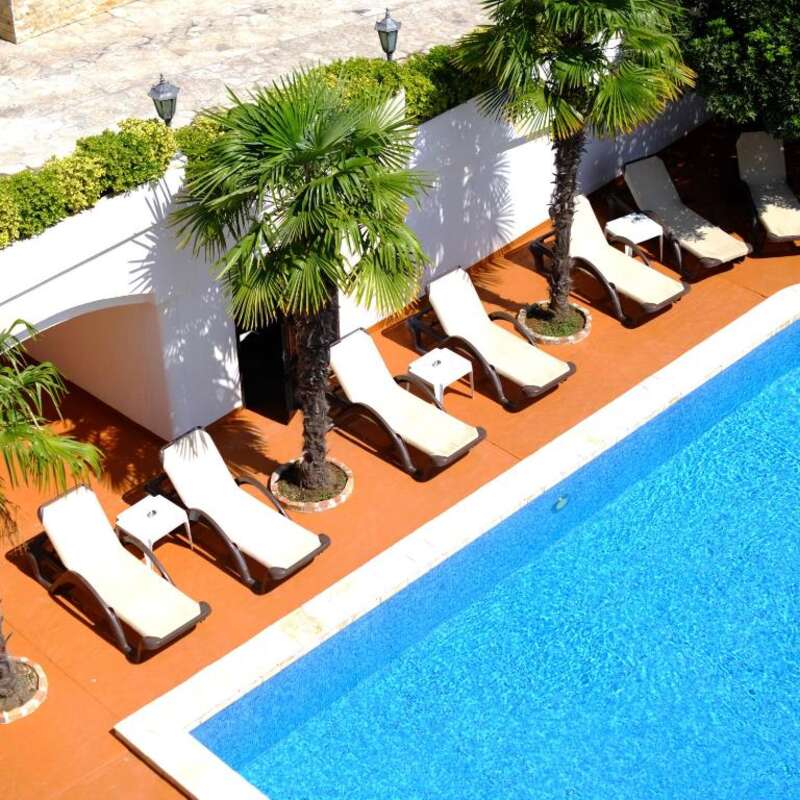 Outdoor swimming pool with sun loungers and palm trees at H Kleopatra
